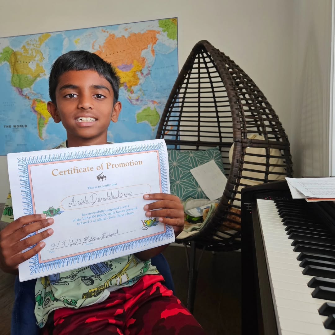 A student holding his certificate of promotion at the piano